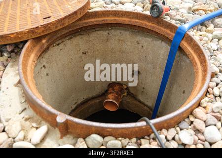 An open sewer manhole. A service cleaning of blocked sewer. A concrete septic tank with a plastic pipe. Rinse and pumping water out. Maintenance work Stock Photo
