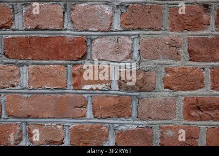 Weathered red bricks form a textured wall. Grey mortar joints show age and wear. Surface reveals subtle cracks and uneven edges. Ideal for architectur Stock Photo