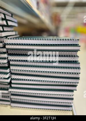 A stack of spiral notebooks with green covers and white pages displayed on a shelf in a stationery store, with colorful supplies in the background Stock Photo