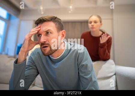 Frustrated angry husband sitting on sofa irritated by wife unstoppable blaming and arguments Stock Photo
