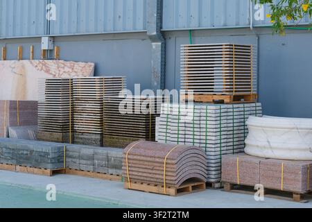 Natural stone slabs, granite pavers and marble elements stacked on pallets in an outdoor construction materials yard. Stock Photo