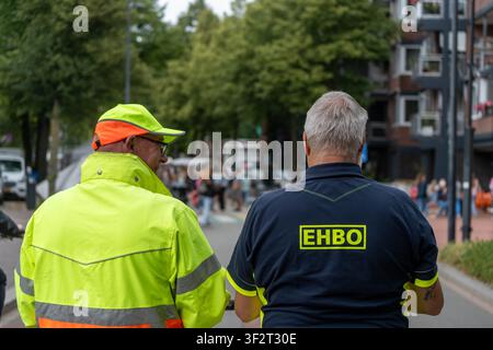 Two men stand side by side on a city street, wearing high-visibility uniforms. Stock Photo