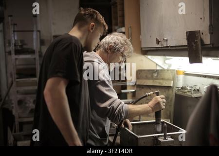 Older mentor teaches young apprentice in workshop Stock Photo