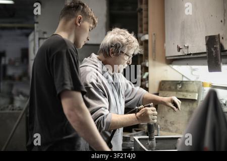 Senior craftsman teaches young apprentice in workshop Stock Photo