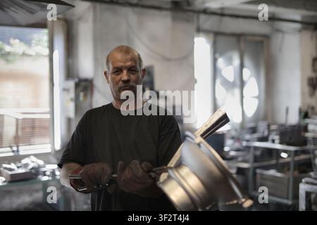 Mature worker with mustache looks at camera in workshop Stock Photo