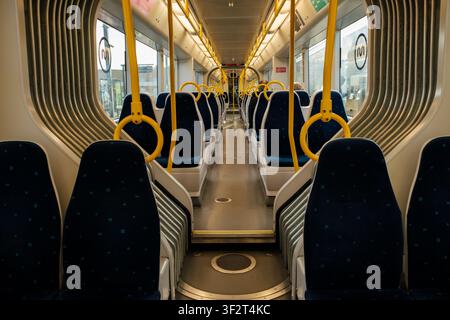 Clean train interior with rows of blue seats and yellow handrails, ready for public transportation Stock Photo