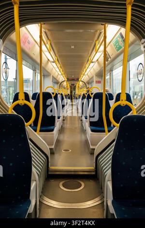 Clean metro train interior with rows of blue seats and yellow grab handles Stock Photo