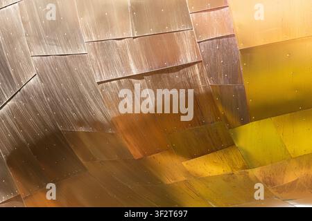 Abstract close-up of curved metallic architectural panels with warm reflections and geometric surface patterns. Stock Photo