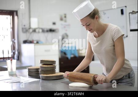 Young female baker rolling out fondant in kitchen Stock Photo