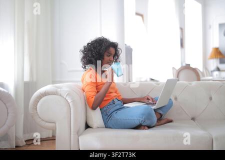 Young black woman relaxing on couch using laptop at home Stock Photo