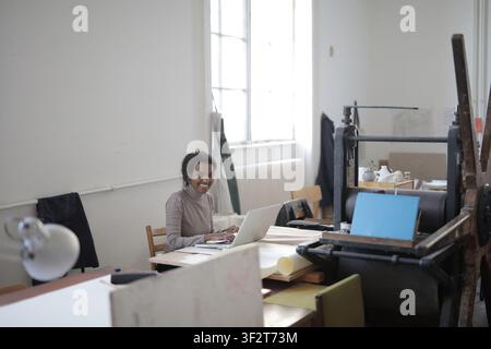 Smiling woman works on laptop in creative studio Stock Photo