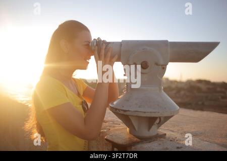 Smiling woman looking through scenic viewer at sunset Stock Photo