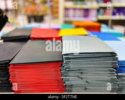 Colorful paper envelopes in shades of red, black, blue, yellow, and gray are stacked neatly on a table inside a stationery store Stock Photo