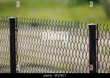 A wire mesh fence with metal posts in front of a green field Stock Photo