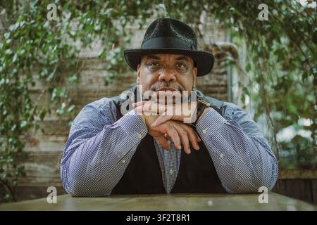 Thoughtful Black man in a fedora hat sitting outside Stock Photo