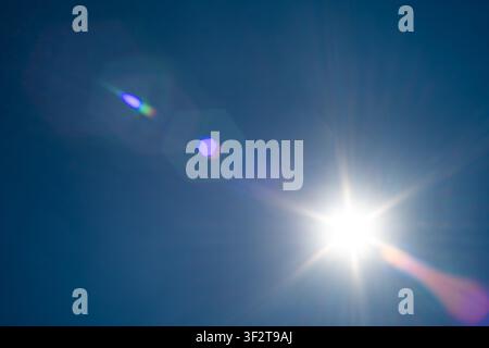 Brilliant sunlight bursts through a cloudless blue sky, creating vivid optical lens flares and radiating long rays of light across the open atmosphere Stock Photo