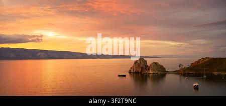 A wide panoramic landscape of a vibrant sunset over a still lake. The sky is filled with soft orange and pink clouds, reflecting on the water's surfac Stock Photo