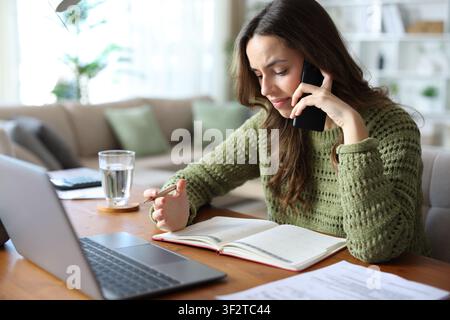 Stressed teleworker talking on phone checking agenda working at home Stock Photo
