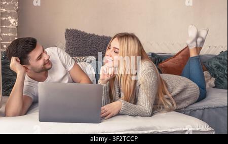Young happy couple on sofa discussing what to buy with laptop Stock Photo