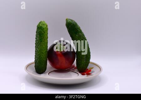 Black tomato and two cucumbers on a plate isolated on a white background Stock Photo