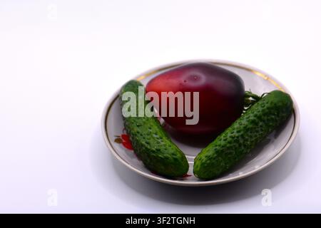 Black tomato and two cucumbers on a plate isolated on a white background Stock Photo