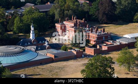 Aerial view of the Wellcome Genome Campus featuring historic red brick buildings, a modern circular glass-roofed structure, and surrounding parkland i Stock Photo