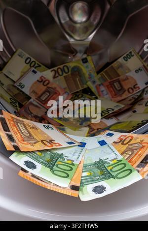 Many euro bills of different denominations lie inside metal drum of automatic washing machine showing creative concept of money laundering. Stock Photo