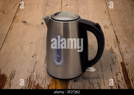 Used matt silver metal electric kettle for water heating with a large black plastic handle, water level indicator and on/off switch on a wooden table Stock Photo