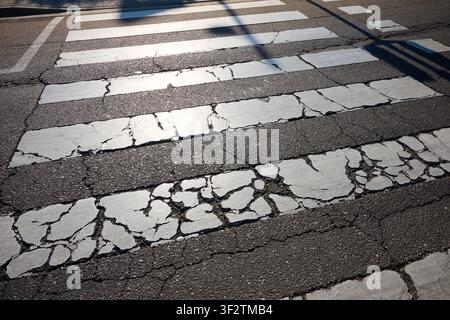 Closeup of an old and worn European zebra crossing that needs repair. White stripes worned an cracked. Stock Photo