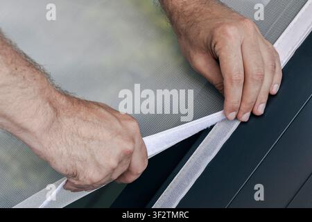 Person adjusting a mosquito screen on hook and loop tape on a window frame, illustrating home maintenance and practical DIY work. Stock Photo