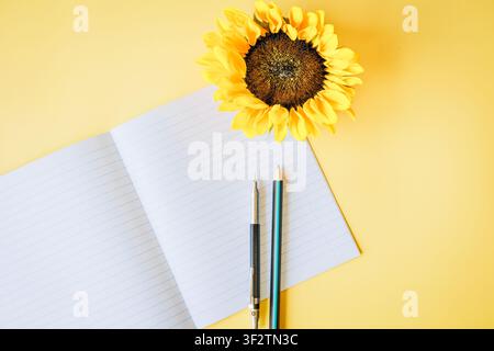 Open lined notebook, writing tools and a sunflower arranged on a yellow indoor desk, creating a bright, cheerful atmosphere of studying, creativity an Stock Photo