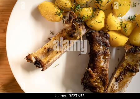 Barbecue ribs with potatoes and dill served on a wooden table, creating a home atmosphere with casual comfort food. Stock Photo