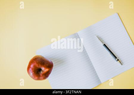 Open lined notebook with a mechanical pencil and red apple on a yellow indoor desk, creating a calm educational background with a fresh atmosphere and Stock Photo