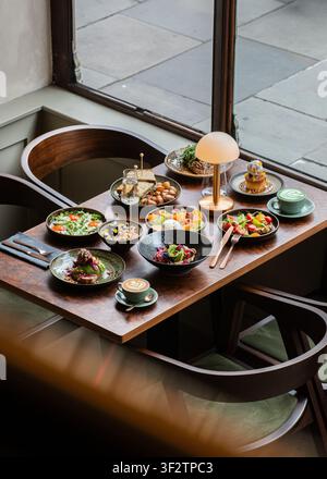 High angle view of a rich brunch table layout with diverse dishes, coffee, and a lamp next to a window. Stock Photo