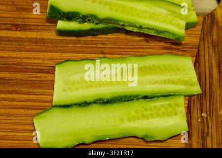 close up of a cucumber cut into thin slices to be used for a hamburger on a wooden chopping board Stock Photo