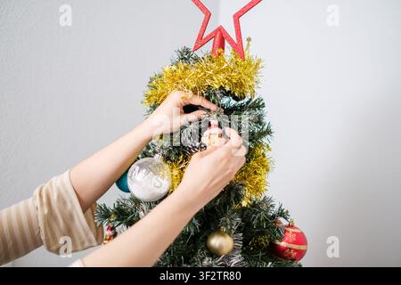 Person decorating a festive christmas tree with various ornaments and a star topper Stock Photo