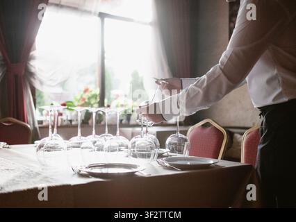 Waiter Setting Up Dining Table In Restaurant Interior Preparing Wine Glasses For Dinner Service Professional Hospitality Service Staff Catering Event Stock Photo