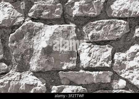 Detailed texture of light grey stone wall made of rough masonry blocks with mortar joints in bright sunlight for architecture background or backdrop. Stock Photo