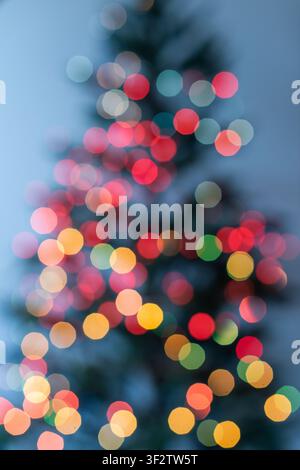 Vertical festive background featuring large warm bokeh circles on a Christmas tree. Yellow, orange, red and green defocused lights with dark blue back Stock Photo