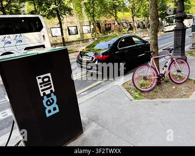 Paris, France - May 14, 2026: Pink bicycle locked beside a curb near a black parked sedan and electric Belib charger on a Paris street. Stock Photo