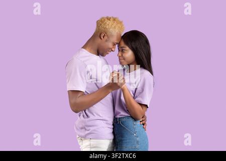 Romantic black couple holding their hands, touching foreheads, being intimate and affectionate on violet background Stock Photo