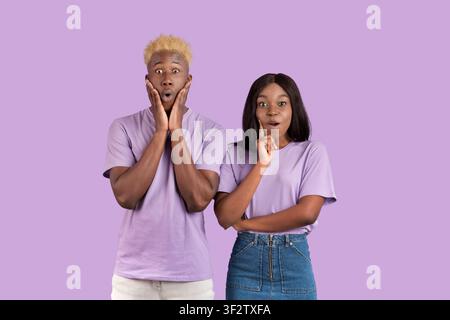 Young black guy and his girlfriend feeling shocked to learn about special offer, sale, discount over lilac background Stock Photo