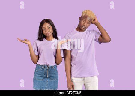 Who knows. Portrait of young black couple shrugging shoulders on violet studio background Stock Photo
