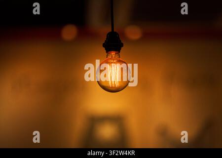 Glowing vintage Edison light bulb hanging against a warm ambient dark background showcasing glowing tungsten filaments Stock Photo