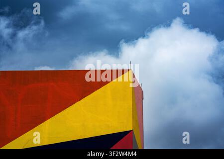 Minimalist low-angle view of a colorful geometric building corner with red and yellow painted panels against dramatic clouds Stock Photo