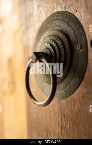 Close-up of an antique brass door knocker with ornate circular plate mounted on a textured wooden door Stock Photo