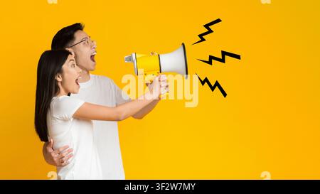 Young asian couple shouting in megaphone over yellow background Stock Photo