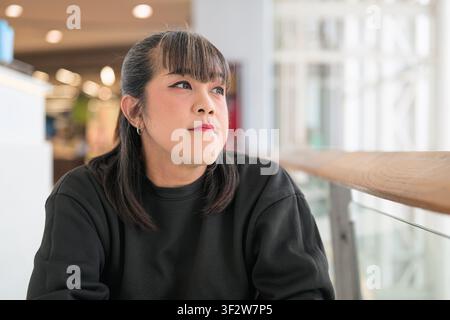 A landscape medium close-up of a Southeast Asian Thai Isan transgender woman looking off-camera with a serene expression. She is seated next to a wood Stock Photo