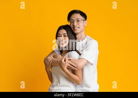 Asian young man in glasses hugging girlfriend from behind Stock Photo