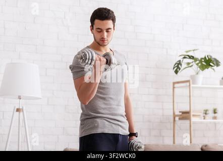 Workout at home. Man with fitness tracker doing exercises with dumbbells in interior Stock Photo